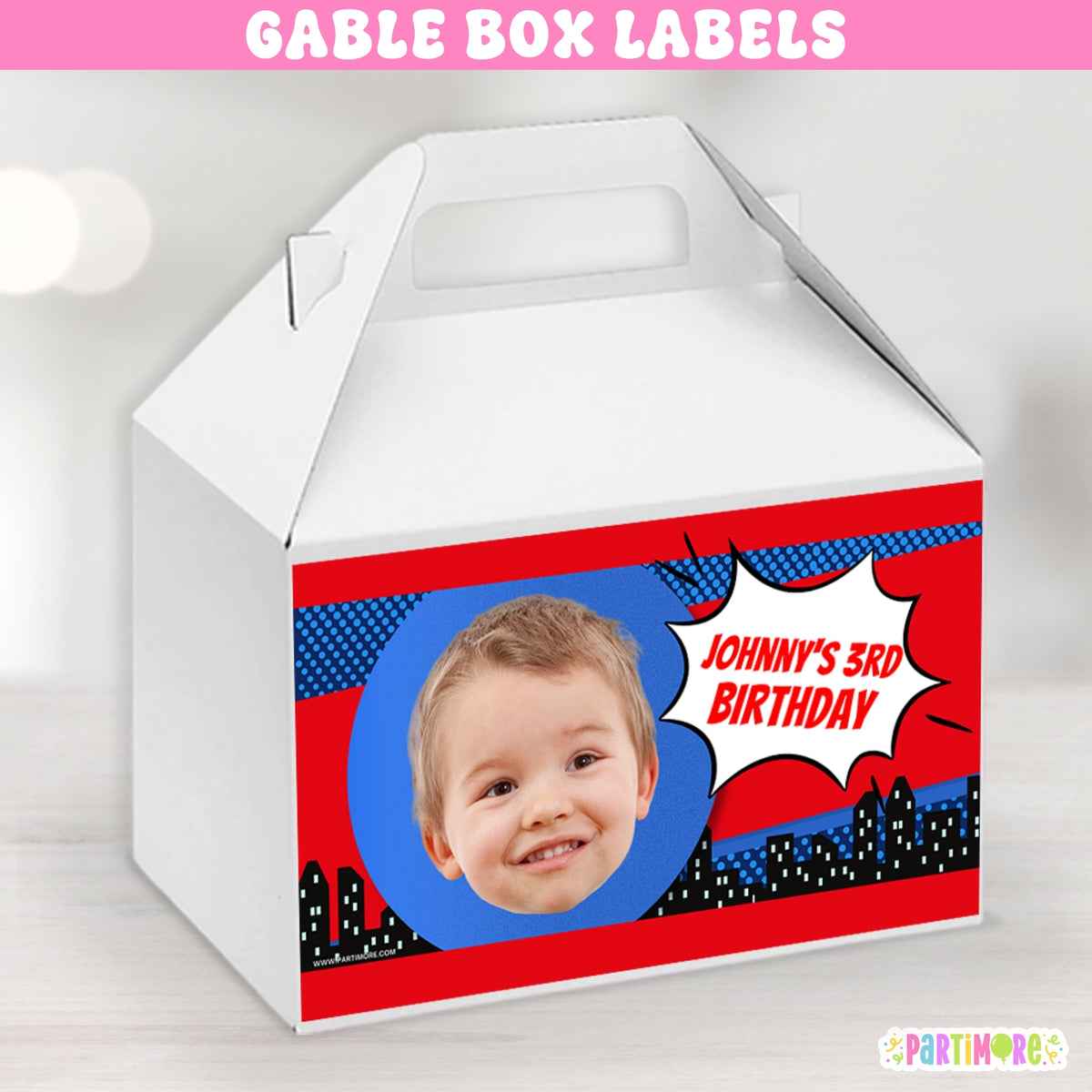 A white cardboard gift box with a custom comic-book style birthday label on the front. The label features a red and blue background with a circular photo cutout of a smiling child and a speech bubble reading JOHNNY'S 3RD BIRTHDAY.